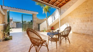 An outdoor patio with wicker furniture, a tiled floor, and a view of a stone wall and gate.