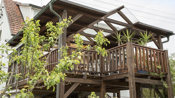 Un balcon en bois avec une balustrade, entouré de verdure.