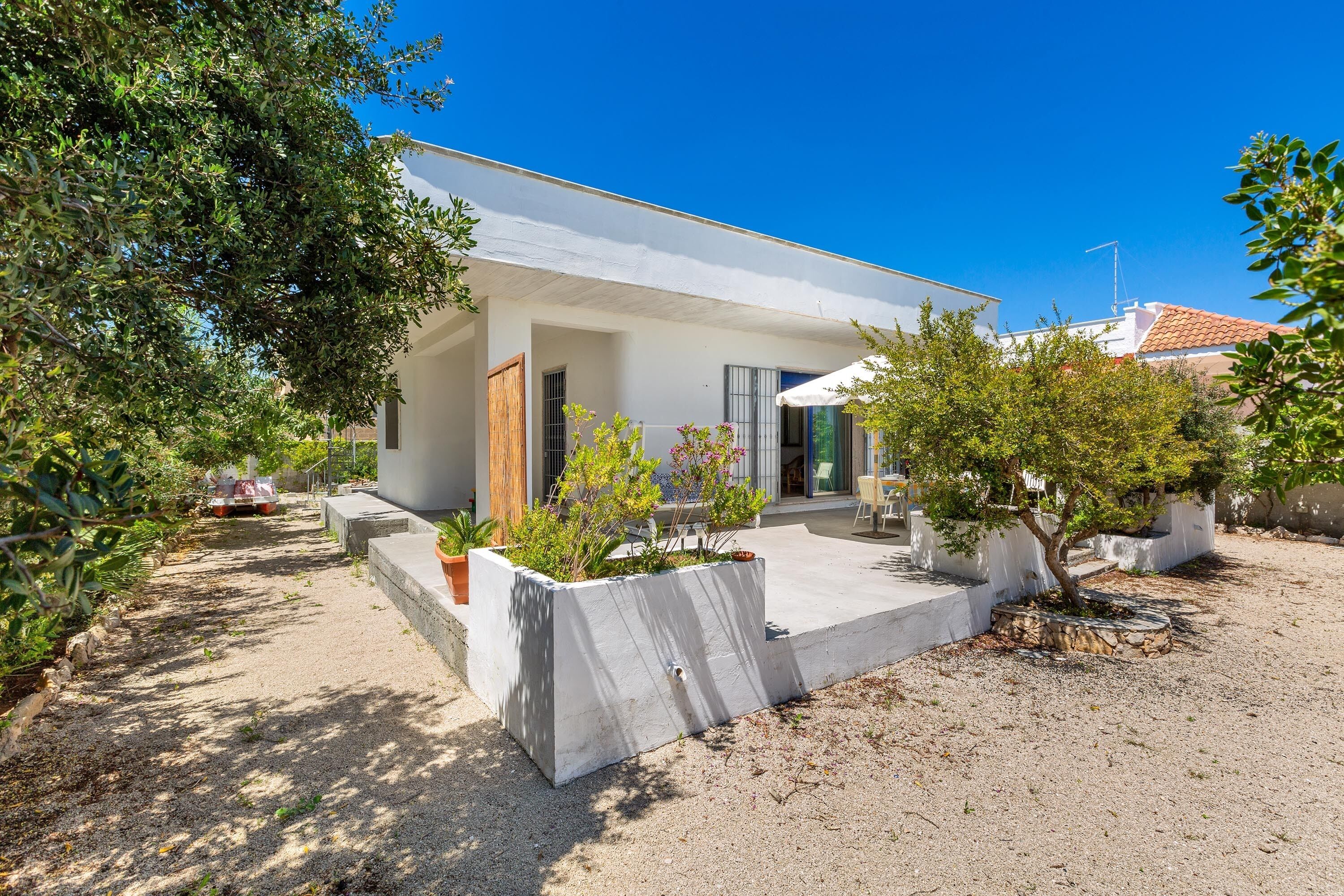 A modern house with a concrete patio, surrounded by trees and a gravel driveway.