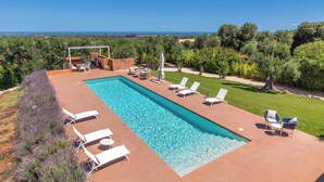 Ein rechteckiger Pool mit weißen Liegestühlen und einem überdachten Sitzbereich.