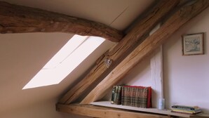 A loft bedroom with exposed wooden beams, a skylight, a wooden shelf with books, and a small chest of drawers. - Chez Sidonie, in the land of Colette. (Treigny-Perreuse-Sainte-Colombe)