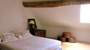 A bedroom with a large bed, a wooden ceiling beam, a nightstand with a lamp, and a window. - Chez Sidonie, in the land of Colette. (Treigny-Perreuse-Sainte-Colombe)
