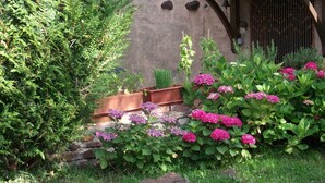 A garden with various plants and flowers, a stone wall, and a wooden structure with a sloped roof. - Chez Sidonie, in the land of Colette. (Treigny-Perreuse-Sainte-Colombe)
