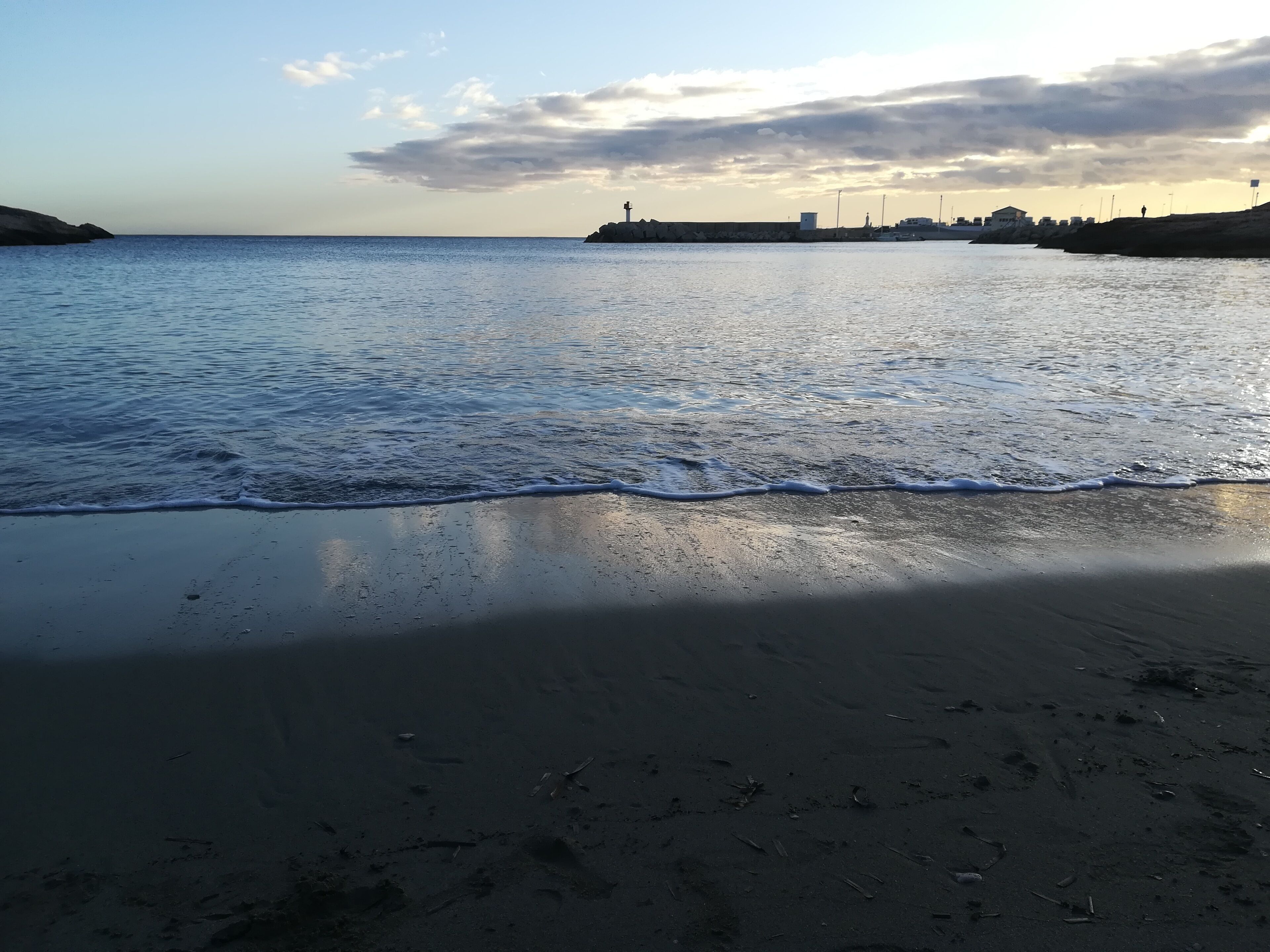Una platja amb ones tranquil·les, cel blau i edificis a la distància.