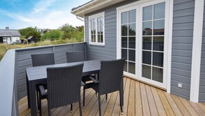 Una terrazza con tavolo e sedie, una porta scorrevole in vetro e una casa grigia sullo sfondo.