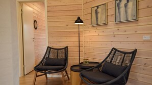 Una stanza con pareti rivestite in legno, due poltrone in vimini con cuscini, un tavolino rotondo, una lampada da terra e due quadri incorniciati.