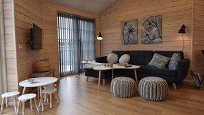 Una camera accogliente in stile chalet, con arredamento in legno, un divano nero, un tavolo da pranzo rotondo e una TV a parete.