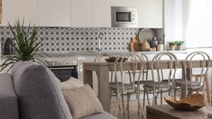 Een moderne woonkamer met een grijze bank, een houten salontafel en een eethoek met witte stoelen en een houten tafel.