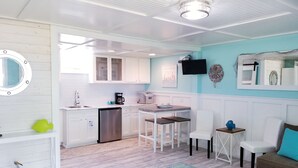 A compact kitchen with white cabinets, a coffee maker, and a microwave. There is a dining area with a table and chairs. - Cozy Studio Condo, short walk to Downtown Saugatuck, courtyard water view (Saugatuck)
