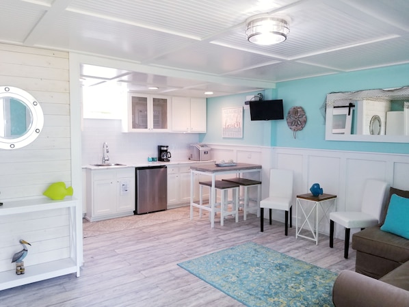 A compact kitchen with white cabinets, a coffee maker, and a microwave. There is a dining area with a table and chairs.