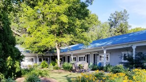 A two-story building with a blue roof, surrounded by lush greenery and yellow flowers. - Cozy Studio Condo, short walk to Downtown Saugatuck, courtyard water view (Saugatuck)