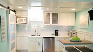 A compact kitchen with white cabinets, a stainless steel dishwasher, a coffee maker, and a toaster. - Cozy Studio Condo, short walk to Downtown Saugatuck, courtyard water view (Saugatuck)