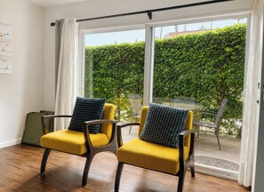 A room with two yellow chairs, a green suitcase, and a sliding glass door leading to a garden. - La Jolla Shores Modern Flat (La Jolla)