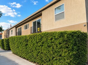 A building with a beige exterior, a well-maintained hedge, and a clear sky.