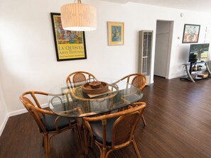 Un coin repas avec une table en verre entourée de chaises en osier, un luminaire suspendu et des œuvres d’art accrochées aux murs.