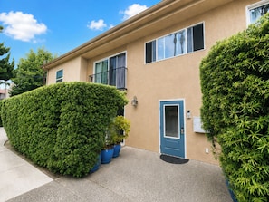 A two-story building with a blue door and windows, surrounded by well-maintained greenery. - La Jolla Shores Modern Flat (La Jolla)