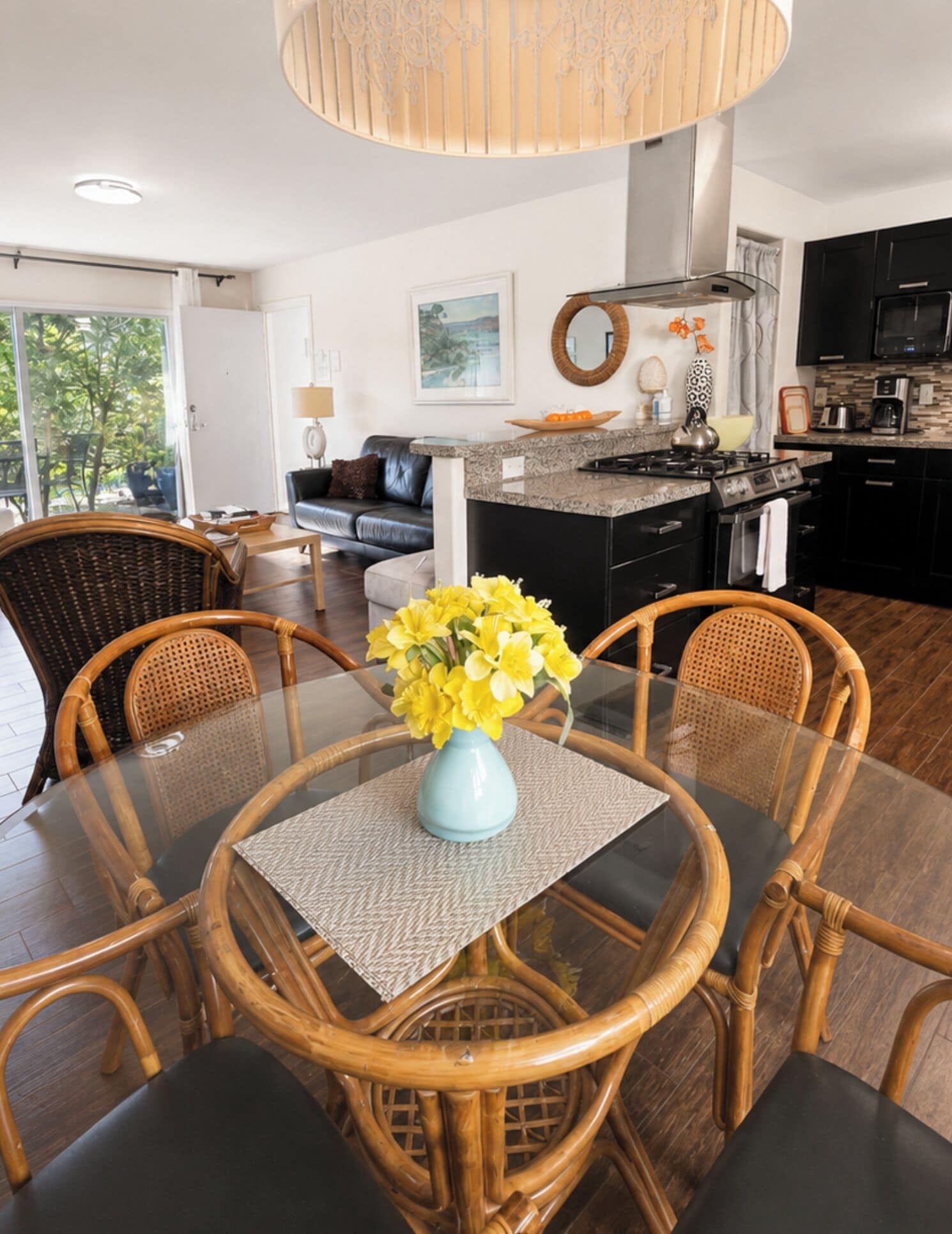 A dining area with a glass table, wicker chairs, and a vase of flowers.