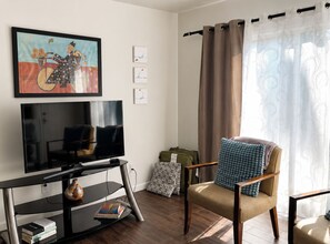 A living room with a television, a chair, a table with books, and artwork on the wall.