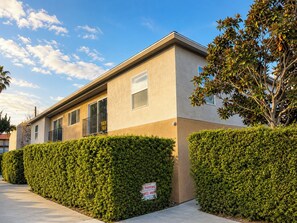 A two-story building with a flat roof, a balcony on the second floor, and a 'No Parking' sign on the hedge.