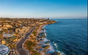 A coastal cityscape with a prominent road running parallel to the beach, residential buildings, and rocky coastline.