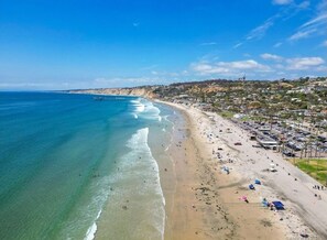 Una playa costera con aguas azules cristalinas, una orilla arenosa y una zona residencial al fondo.
