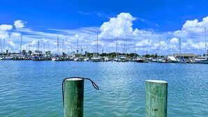 A marina with multiple boats docked, wooden posts in the foreground, and a clear blue sky. - The Sand Piper-Pier, Pool, Bay View & Boat Launch (Rockport)