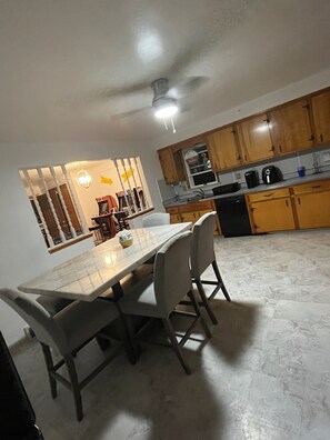 A dining area with a marble table and chairs, wooden cabinets, and a kitchen in the background.