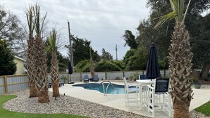 En trädgård med en pool, palmer och utemöbler.
