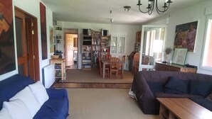 A spacious living room with a blue sofa, a brown sofa, and a wooden coffee table. There is a dining area with a table and chairs, and a kitchen in the background. - CASA SIERRA AVELLANEDA AVILA SPAIN (Avellaneda)