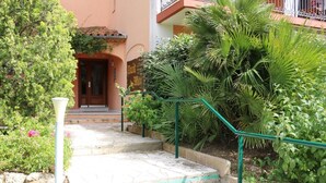 A staircase leading to a building entrance, surrounded by lush greenery and a street lamp. - Seaside apartment (Saint-Aygulf)