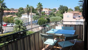 A balcony with a table and chairs, overlooking a residential area with houses and palm trees. - Seaside apartment (Saint-Aygulf)