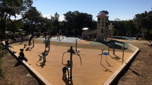 A playground with various play equipment, including swings and climbing structures, surrounded by trees and a building in the background. - Seaside apartment (Saint-Aygulf)