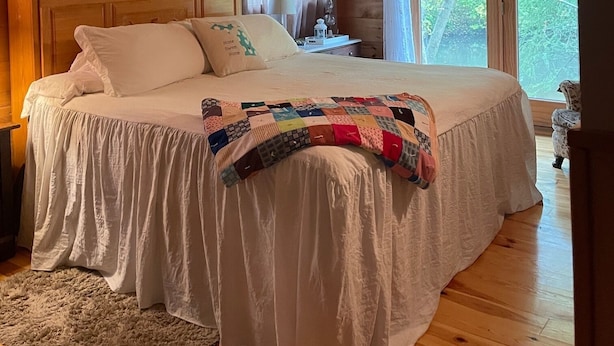 A cozy bedroom with a wooden ceiling, a large bed with white bedding, a quilt, and a nightstand with a lamp. - Unplug and kick back! Simple, relaxing cabin on the Clam River. (Marion)