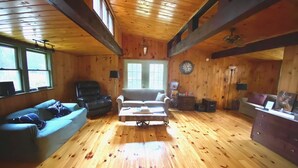 A log cabin interior with a wooden floor, a sofa, a chair, a coffee table, and a clock on the wall. - Unplug and kick back! Simple, relaxing cabin on the Clam River. (Marion)