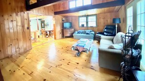 A wooden cabin interior with a dining area, a sofa, a TV, and a ceiling fan. - Unplug and kick back! Simple, relaxing cabin on the Clam River. (Marion)