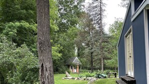 A house with a stone pathway leading to a wooden deck, surrounded by lush greenery and trees. - Unplug and kick back! Simple, relaxing cabin on the Clam River. (Marion)