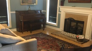 Ein Wohnzimmer mit Klavier, Kamin, Sofa und Sessel.