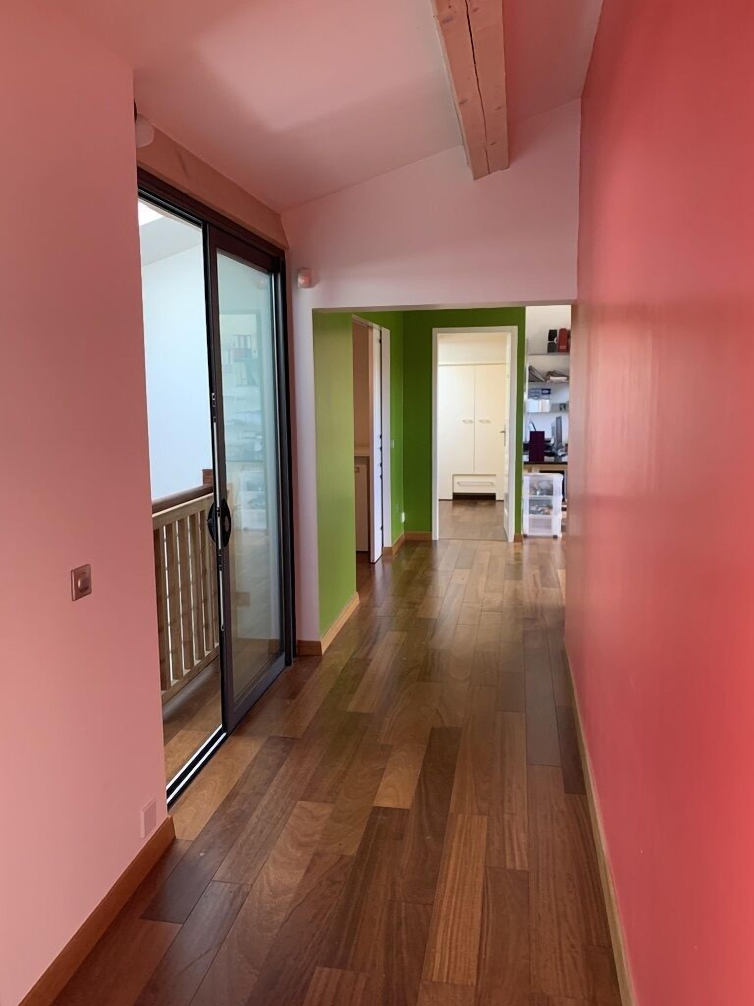Un couloir doté d’un plancher en bois, d’une porte-fenêtre coulissante et d’un mur vert.