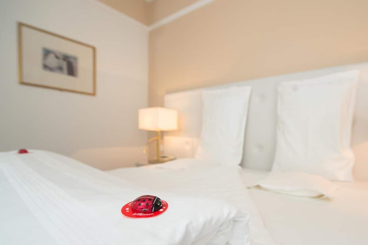 A hotel room with a neatly made bed, a nightstand with a lamp, and a framed picture on the wall.