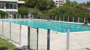 A swimming pool with a metal fence, a lifeguard tower, and a grassy area with a bench.