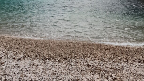 A coastal scene with clear turquoise water, rocky cliffs, and a pebble beach.