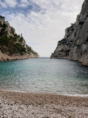 A coastal scene with clear turquoise water, rocky cliffs, and a pebble beach.