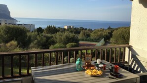 A balcony with a table set for breakfast, overlooking a coastal view with buildings and greenery.