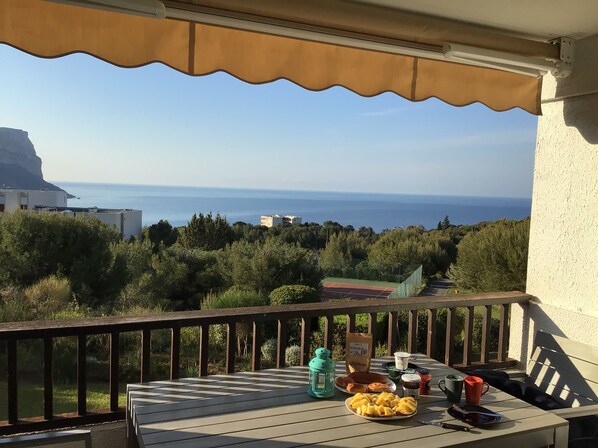 A balcony with a table set for breakfast, overlooking a coastal view with buildings and greenery.