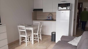 A modern kitchen with white cabinets, a dining area with a white table and chairs, a grey sofa, and a ceiling fan.