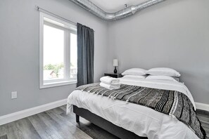 A bedroom with a bed, a nightstand, a lamp, and a window with curtains. - High-end condo downtown Kingston near RMC/Queens (Kingston)