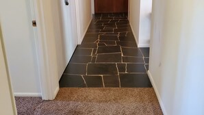 Un pasillo con piso alfombrado, paredes blancas y una puerta de madera al final.