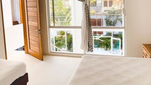 A bedroom with a large window, a wooden door, and a bed with a white quilt.