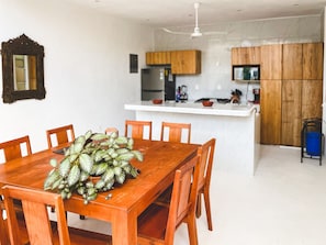 Un coin repas avec une table et des chaises en bois, une cuisine avec des placards en bois et un ventilateur de plafond.