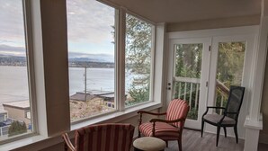 A room with large windows overlooking a body of water and a distant landscape. There are two striped armchairs and a black chair with a woven backrest. - Stunning views of Lake Washington (Seattle)